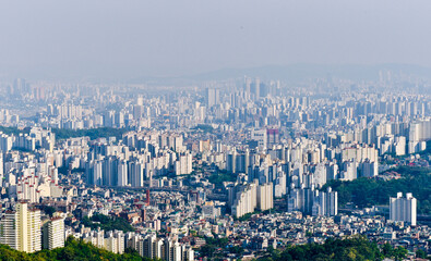A city with many buildings and a large hill in the background. The sky is cloudy and the sun is not visible