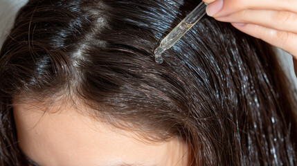 A girlâs parted hair illuminated by warm studio lighting as a pipette dispenses growth-enhancing oil onto her scalp, highlighting texture, shine, and health