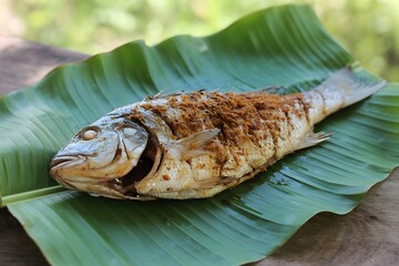Whole fried fish with spices served on a banana leaf, close up view