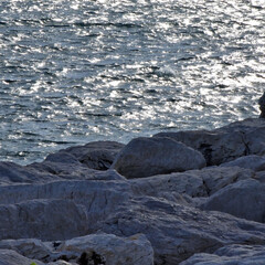Close-up view of rocky shoreline on the Tyrrhenian Sea near Naples. Natural stone texture with gentle water movement creating a calm coastal atmosphere.
