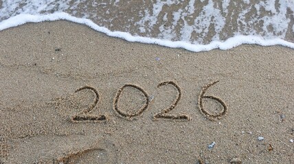 close up of year 2026 numbers written on the sand on the beach with waves and water in daytime