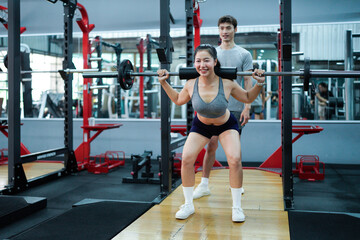 Professional fitness trainer guiding female athlete performing precise barbell squats in modern gym setting. Motivation and healthy lifestyle concept
