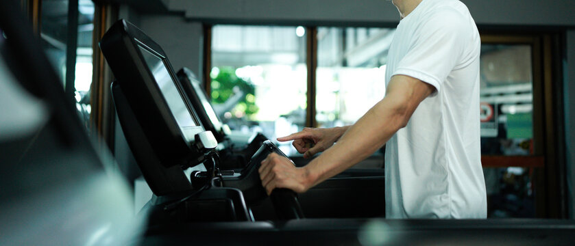 Man's finger adjusts settings, increasing speed or starting a workout in a fitness center.