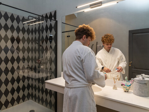 Man in a bathrobe brushing his teeth in the bathroom in the morning - Powered by Adobe