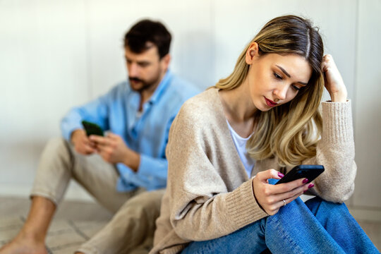 Young couple sitting back to back, both focused on their smartphones, appearing emotionally distant