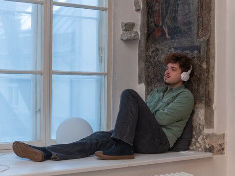 Man sitting on a window sill and listening to music