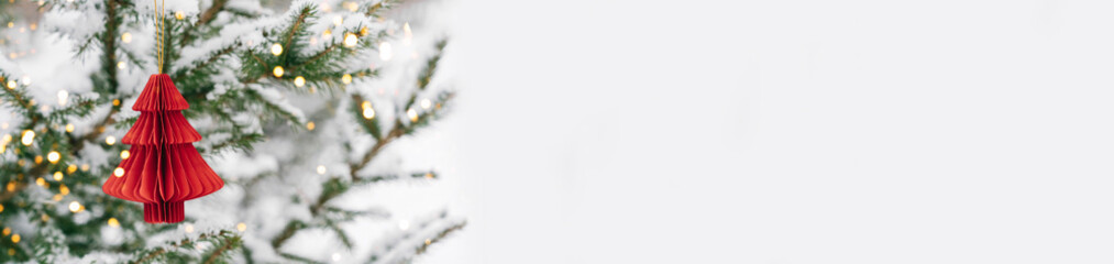 Minimalist Christmas tree with red paper ornament and lights on snowy background. Festive composition, layout for a New Year's card, banner