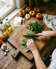 Hands Chopping Fresh Basil for a Caprese Salad on a Rustic Wooden Board.