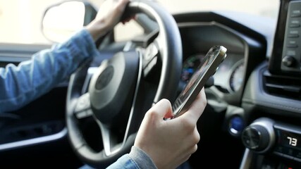 Closeup of distracted woman's hands using mobile phone while driving a modern car, texting and scrolling, an illegal, unsafe and dangerous behavior on a road, that can cause a tragic accident.