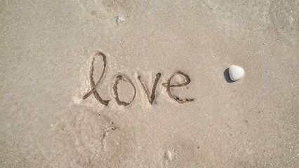 Love written in the sand with a shell nearby on the beach.