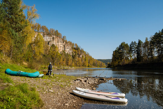 Experience the tranquil beauty of a serene autumn riverbank scene adorned with paddleboards and kayaks gliding peacefully under a clear blue sky, creating a picturesque moment in nature