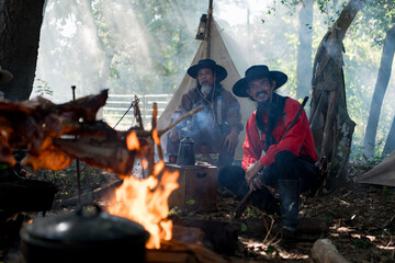 Group of cowboys preparing food at a campfire, roasting meat together in a warm