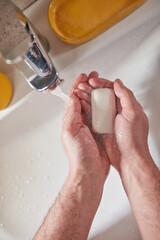 Human hands are turning the home faucet on and washing it with soap and clean tap water for good personal hygiene.