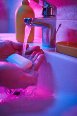 Human hands are turning the home faucet on and washing it with soap and clean tap water for good personal hygiene.