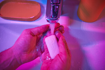 Human hands are turning the home faucet on and washing it with soap and clean tap water for good personal hygiene.