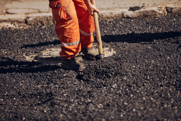 Construction worker working on a new asphalt layer on a public street.