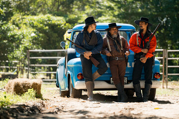 A group of cowboys laughing together around a vintage pickup truck © Wosunan