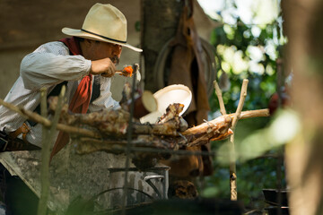 A cowboy preparing food at a rustic outdoor campfire, seasoning and stirring a steaming soup pot