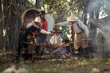 Group of cowboys preparing food at a campfire, roasting meat together in a warm
