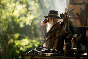 A senior cowboy stands beside a food cart, drinking coffee