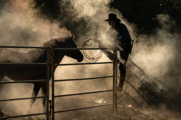 A cowboy training a horse in a dusty corral at sunrise, creating a dramatic western silhouette