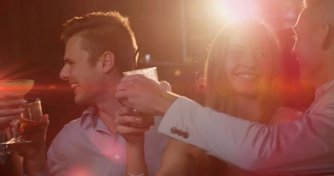 Four friends clinking drinks in nightlife bar, man on right offering toast, lens flares overlapping