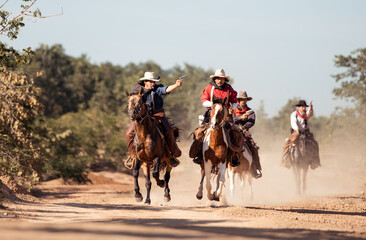 Obraz premium Group of cowboys riding at horse on a dusty trail, with raising a revolver during a western chase scene
