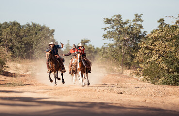 Obraz premium Group of cowboys riding at horse on a dusty trail, with raising a revolver during a western chase scene
