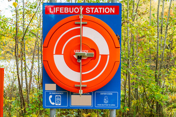 Lifebuoy Station containing a life saving ring or emergency life saver buoy at the edge of a lake, behind trees