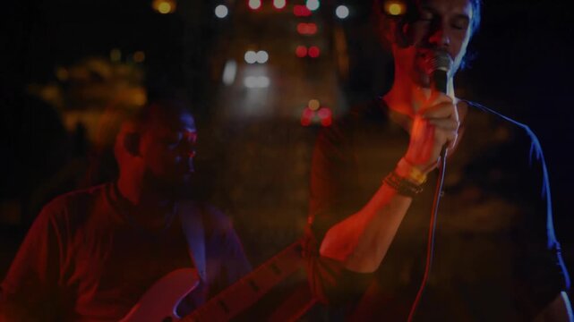 Singer adjusting mic grip then singing for music while bassist plucking, lights drifting over stage