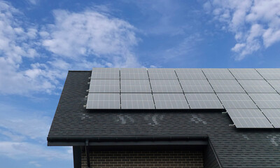 Fototapeta premium Solar panels on house roof against blue sky with clouds