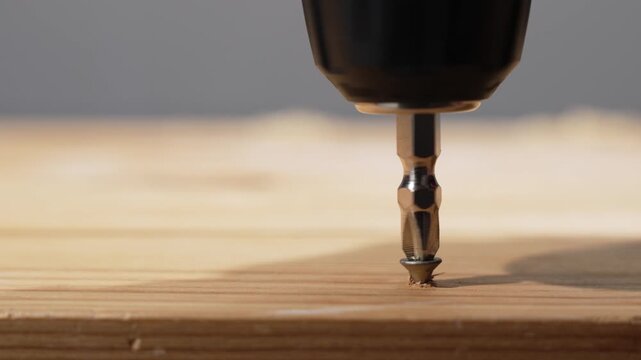 Driver bit spins a wood screw into a board, tightening it down. Macro shot shows metal threads biting into timber.