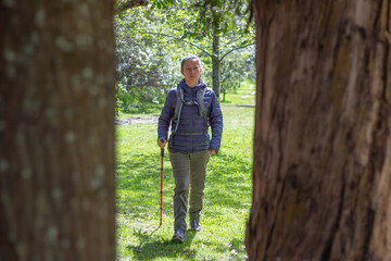 Woman hiking through green park with trekking pole