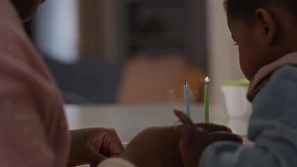 Close-up of young Black mother and her toddler daughter blowing candles on birthday cake together and clapping hands