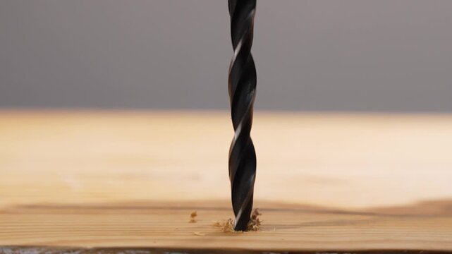 Twist drill bit hovers over a wooden plank, perfectly aligned for the next hole. Shallow depth of field isolates the cutting tip.