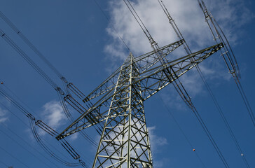 A German electricity pylon stands against a clear blue sky, showing the power transmission network. The steel mast supports the electric grid and the energy transition.
