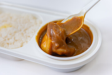 白い弁当容器に入ったカレーをスプーンで持ち上げたクローズアップ