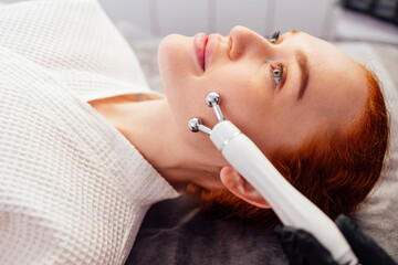 Red-haired woman receiving facial treatment with a modern device in a spa setting, showcasing relaxation and skincare techniques for rejuvenation and beauty enhancement