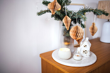 Festive holiday decor featuring a small Christmas tree adorned with paper ornaments, candles, and a charming miniature house, creating a warm and inviting atmosphere for seasonal celebrations