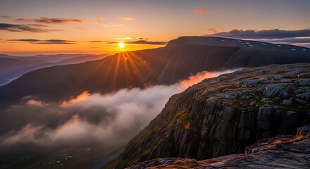 Sun rays bursting over the mountain range at sunset with clouds below