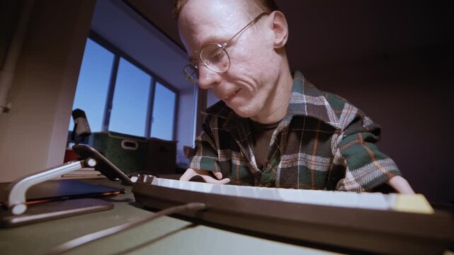 Man with a physical disability using a computer and smartphone at his desk in a dimly lit room