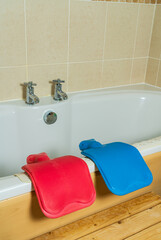 Pink and blue hot water bottles on the side of a bath, winter warmth and cozy themed or muscle relaxation/pain relief concepts