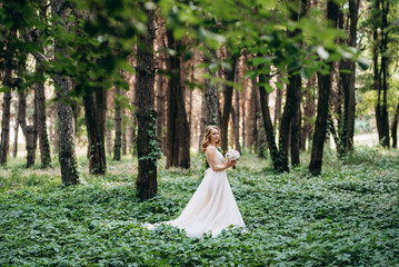 Blonde bride in a light coral dress in a green forest