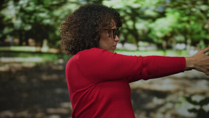 Woman with clasped hands and closed eyes wearing red sweater standing in green forest clearing; serenity mindful reflection.