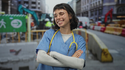 Naklejka premium Woman doctor in blue scrubs points finger to object at construction site outdoors with yellow stethoscope around neck; determination.