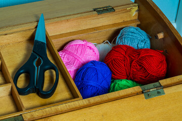 Ball of different coloured wool in a wooden knitting box with a pair of scissors, hobby concept