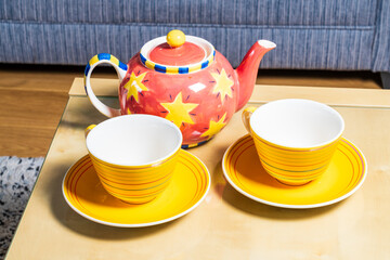 Two yellow cups and a bright colourful teapot in a living room setting, home comfort and relaxation concept