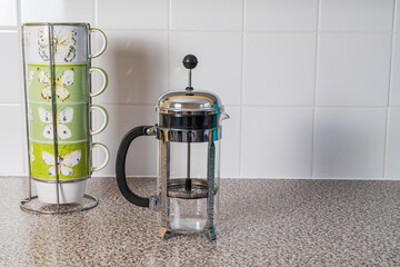 Rack of green coffee mugs and a glass cafetiere in a kitchen setting