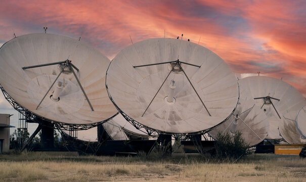Large satellite dishes facing sunset sky in a telecommunications facility