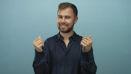 Man smiling showing hands with pinched fingers gesture against light blue studio wall; playful invitation.